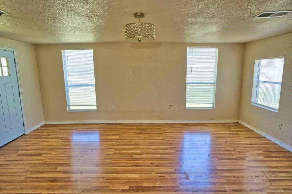 This cozy living area features laminate wood flooring, neutral walls, and ample natural light from windows. A comfortable seating arrangement faces the entry door, providing a welcoming atmosphere.