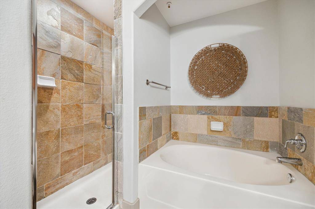 The bathroom features a modern design with a combination of a glass-enclosed shower and a separate soaking bathtub.