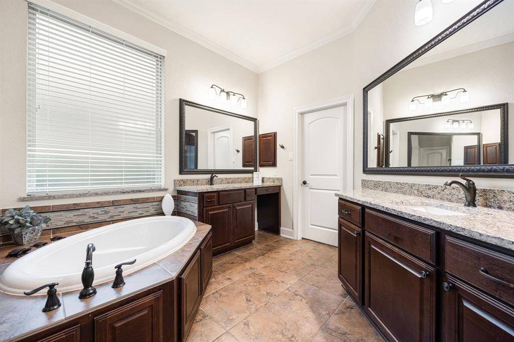 This primary bathroom is definitely move-in ready! Featuring a separate garden tub for soaking after a long day with custom tile detailing, two separate vanities, dark stained cabinets with granite countertops, spacious walk-in closet with shelving, high ceilings, neutral paint, sleek and dark modern finishes.