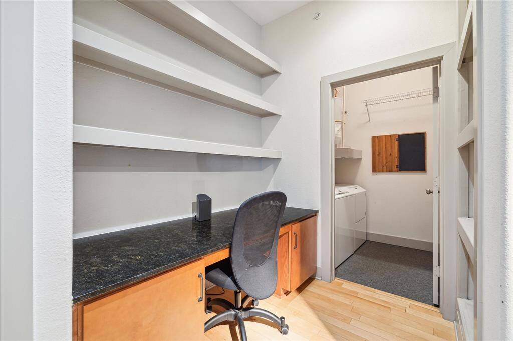 This efficient workspace leads to a separate laundry room and features a spacious desk, ample cabinets, and shelving—perfect for keeping work and chores distinct from living areas.
