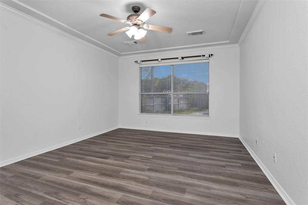 This room features elegant laminate wood flooring, a large window with blinds for natural light, and a ceiling fan, offering a spacious and inviting atmosphere.