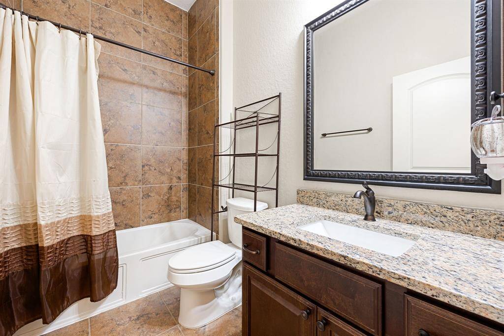 Secondary bath features tile flooring, bath/shower combo with tile surround, dark wood cabinets, beautiful granite countertops, mirror, dark, sleek fixtures and modern finishes.