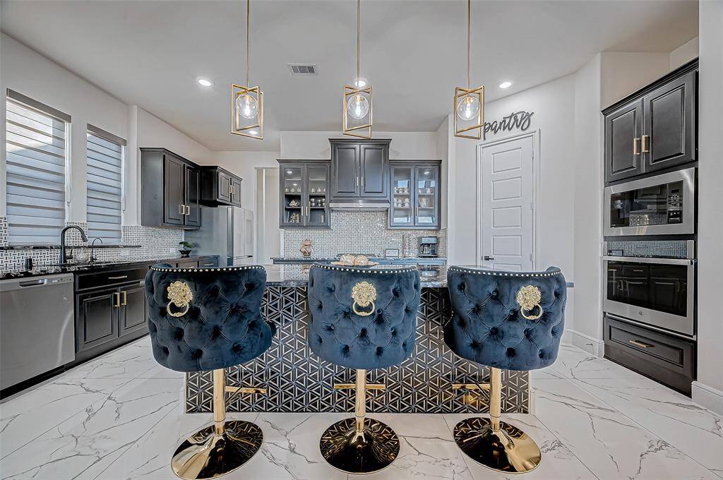 Gourmet KitchenA chef’s delight, the expansive kitchen boasts a massive center island illuminated by hanging pendant lights. Marbled quartz countertops, rich dark cabinetry with gold accents, and a striking black-and-white tile backsplash create a bold yet inviting ambiance. Complete with stainless steel appliances, a butler pantry, and abundant storage, this kitchen is as functional as it is beautiful.