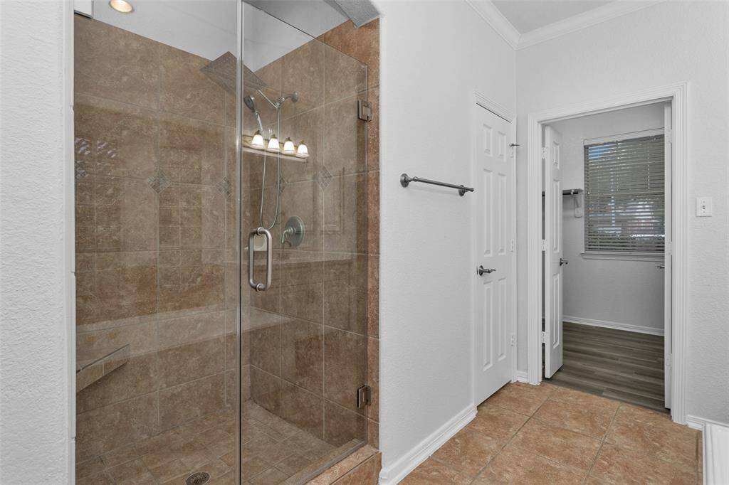This spacious bathroom featuring a large, glass-enclosed shower with elegant tilework. Adjacent is a doorway leading to the primary closet with a window, allowing natural light. The floor is tiled, providing a clean and modern look.