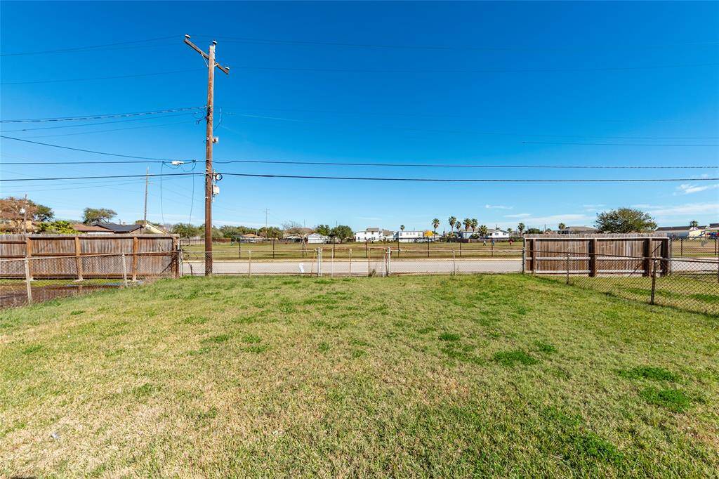 Spacious backyard with a well-maintained lawn, enclosed by a chain-link fence, offering a clear view of the street and surrounding neighborhood. Ideal for outdoor activities and pets.