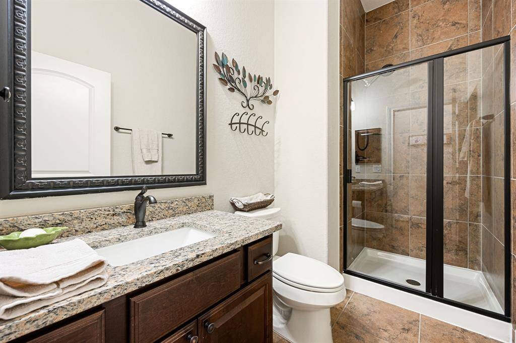 Secondary bath features tile flooring, black framed walk-in shower with tile surround, dark wood cabinets, beautiful granite countertops, mirror, dark, sleek fixtures and modern finishes.