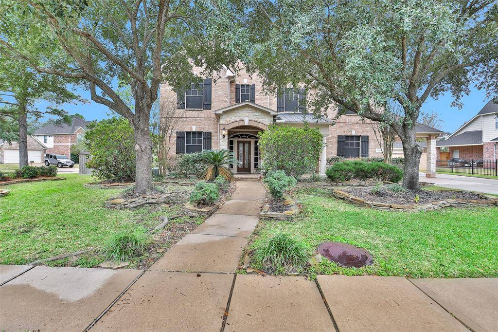 Charming two-story brick home with a welcoming front porch, framed by mature trees and well-maintained landscaping. The pathway leads directly to the entrance, offering great curb appeal in a suburban neighborhood setting.
