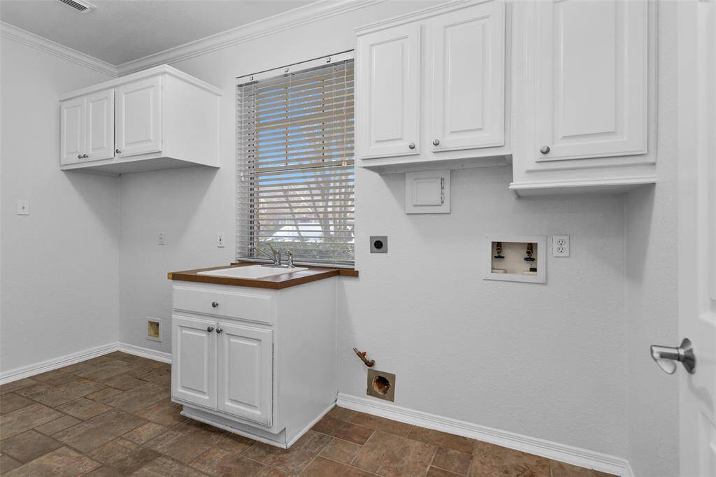 The bright, clean laundry room with white cabinetry, a utility sink, and space for a washer and dryer. The room has tiled flooring and a window with blinds, providing natural light.