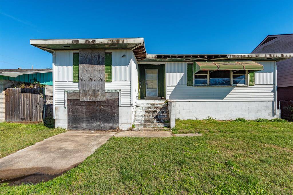 This photo shows a fixer-upper home with a boarded-up garage, steps leading to the entrance, and a green lawn. The exterior is in need of maintenance, offering potential for renovation and personalization.