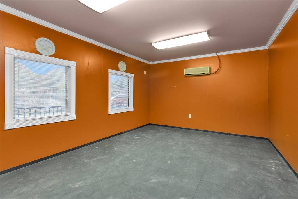 This extra room features vibrant orange walls with two large windows, providing natural light. It includes a wall-mounted mini split and overhead lighting, offering a spacious area suitable for various uses.  If you need a 3rd actual garage it can be turned back into garage space.