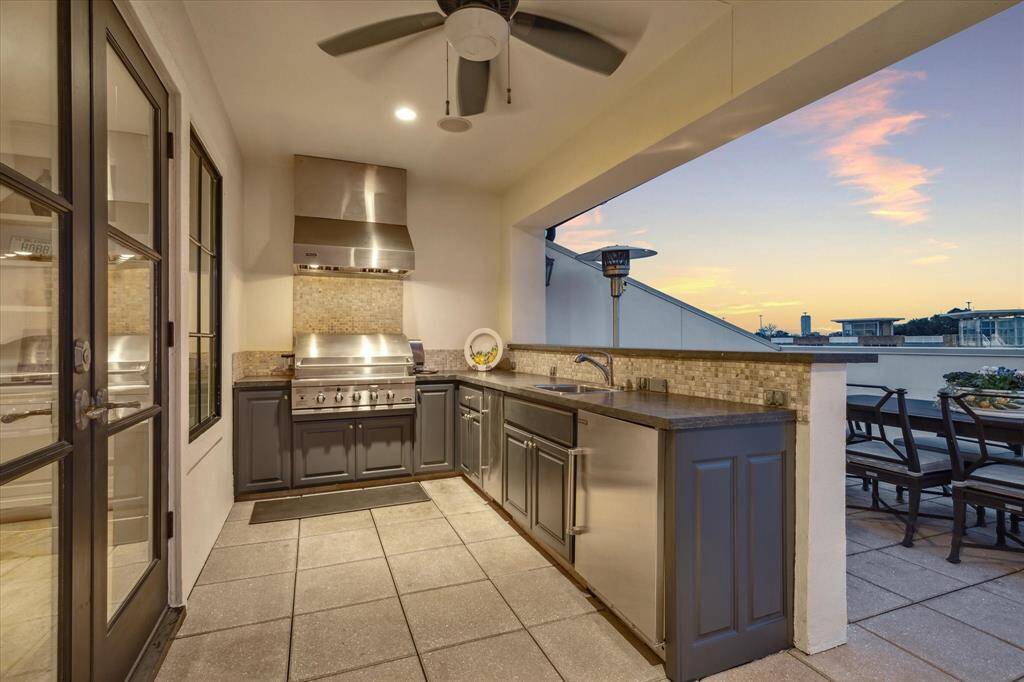 Outdoor kitchen fully equipped with gas grill, vent hood, stainless sink, ice machine & beverage refrigerator.