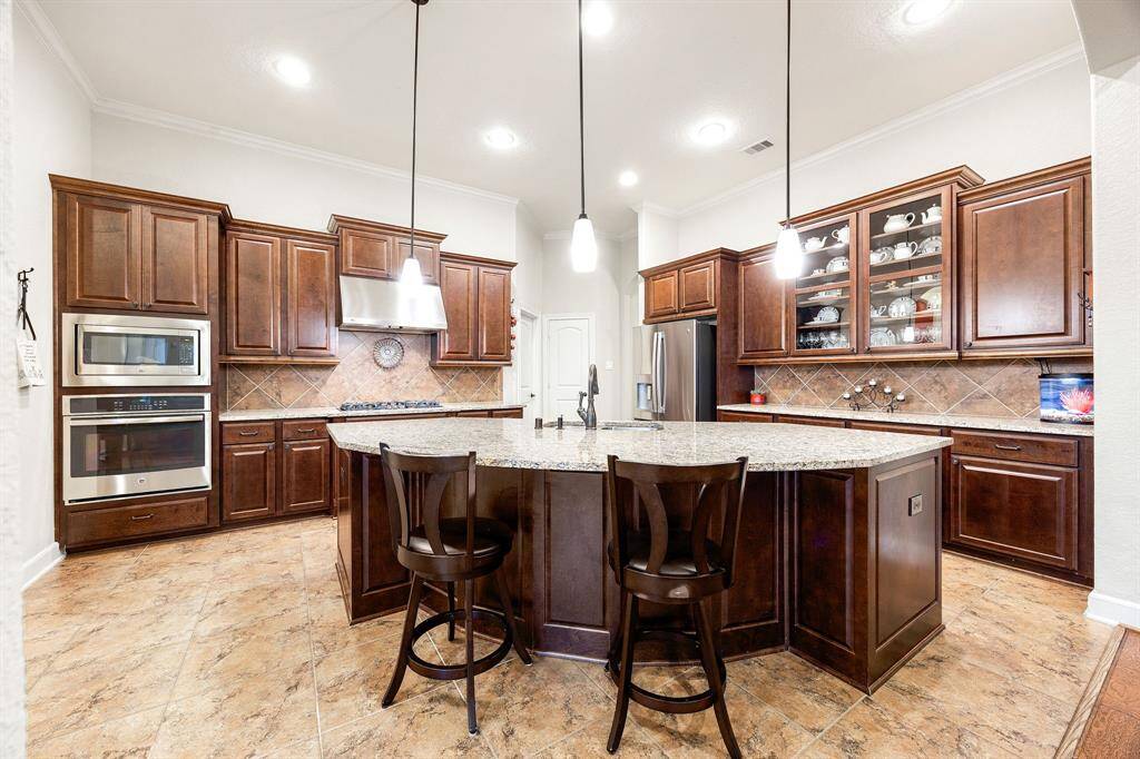 This kitchen is by far any chef’s dream! This spacious kitchen features high ceilings, dark stained wood cabinets, granite countertops, SS appliances, tile backsplash, recessed lighting with additional custom pendant lighting, granite kitchen island with sink and space for breakfast bar and a walk-in pantry all overlooking your huge family room.