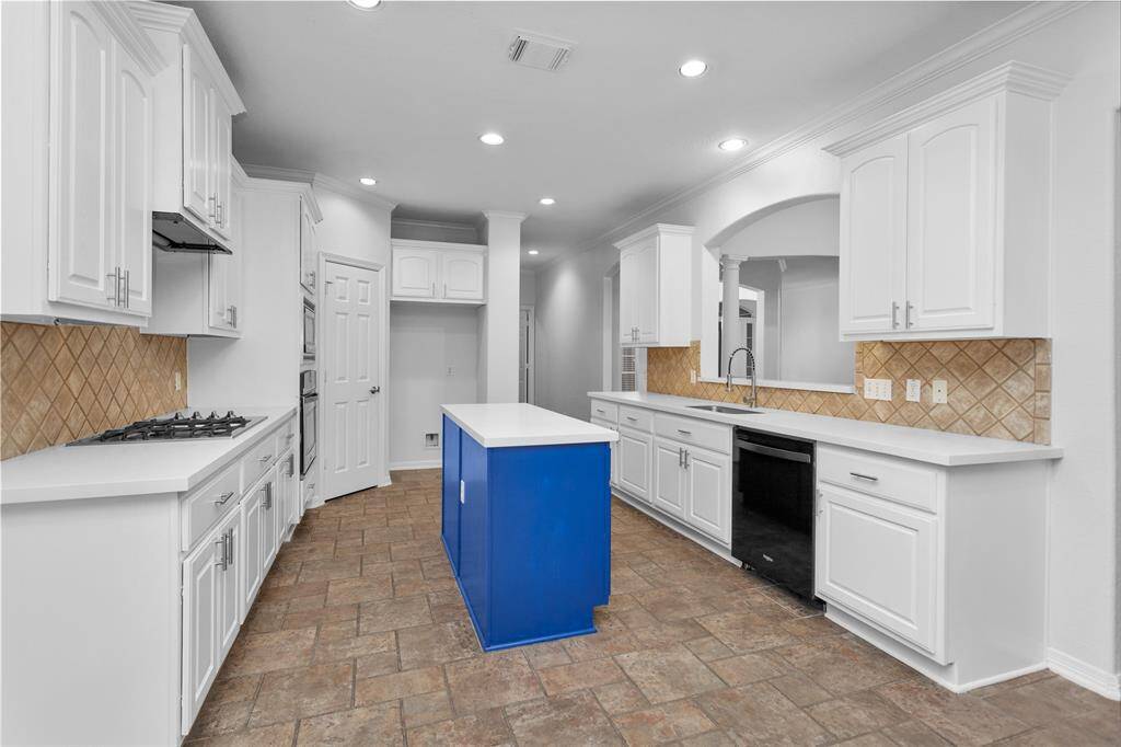 This spacious kitchen features modern white cabinetry, a bold blue island, and a gas stove. It includes ample counter space, a tiled backsplash, and recessed lighting, creating a bright and functional cooking area.