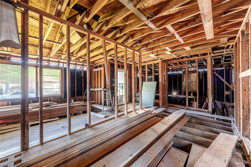 This photo shows a house under renovation, featuring exposed wooden framing, open walls, and ceiling beams. It's a work-in-progress, ready for customization and finishing touches.