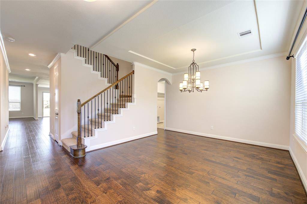 This is a well-lit dining area with hardwood floors, a beautiful chandelier, and a view of a staircase with elegant railing. The open layout connects to other living spaces, providing a warm and inviting atmosphere.