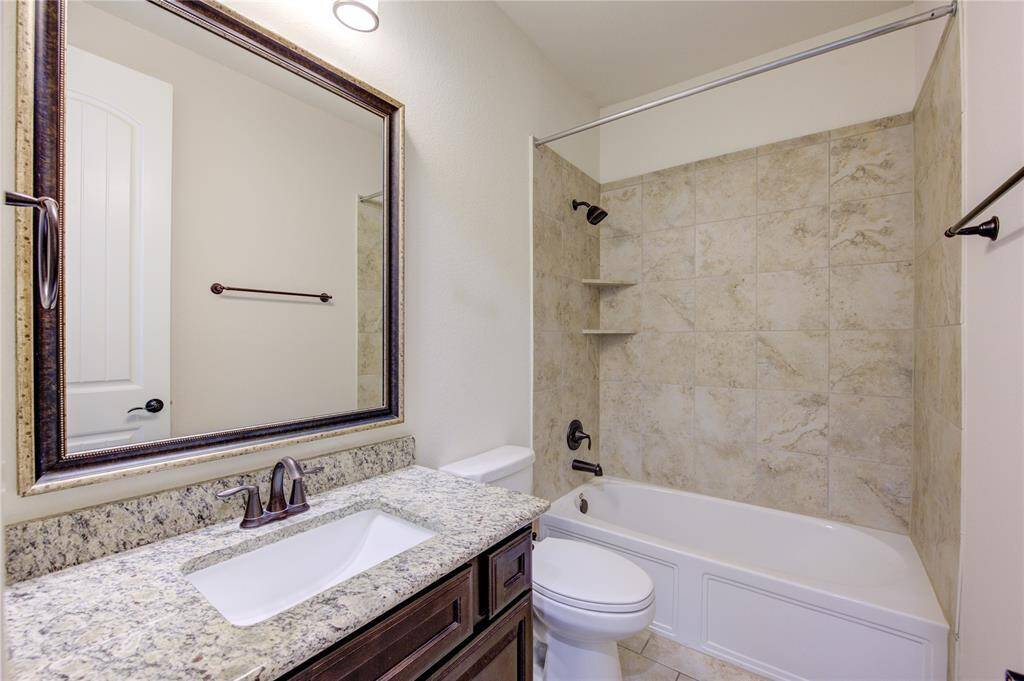 This bathroom downstairs features a modern design with a granite countertop, undermount sink, and dark wood cabinetry. It includes a shower-tub combination with neutral tile surroundings and contemporary fixtures, offering a clean and inviting space.