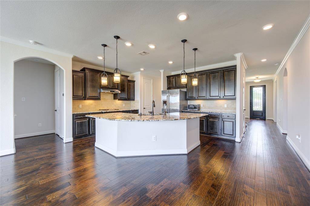 This spacious kitchen features elegant dark wood cabinetry, granite countertops, and a large central island with pendant lighting. The open layout connects seamlessly to the living area, complemented by rich hardwood floors and ample natural light.