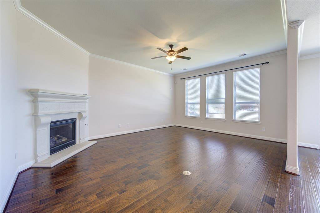 Bright and spacious living room featuring hardwood floors, a corner fireplace, ceiling fan, and large windows with blinds.