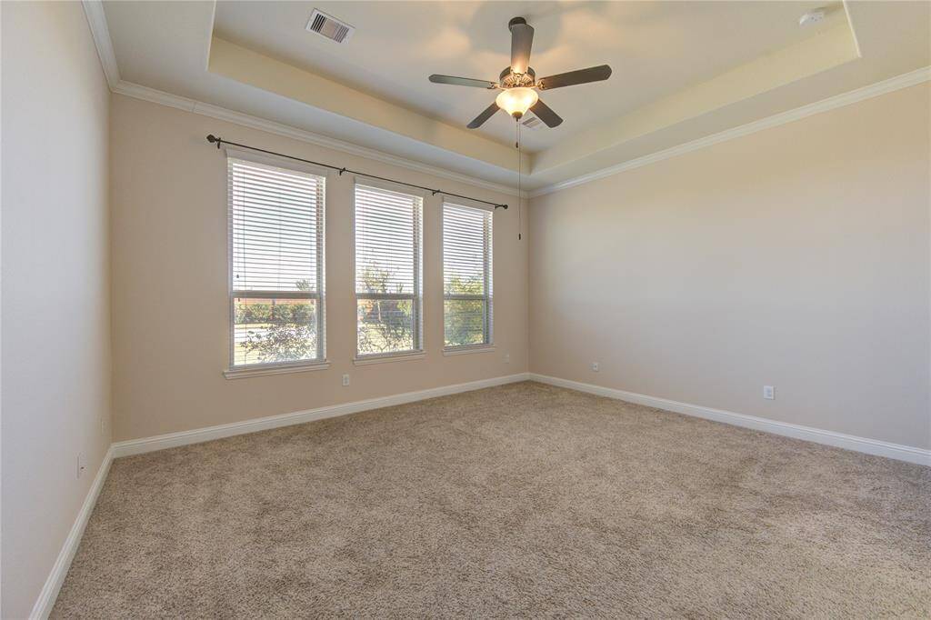 Spacious master bedroom with neutral walls, plush carpeting, and a tray ceiling with a ceiling fan. Three large windows allow ample natural light.