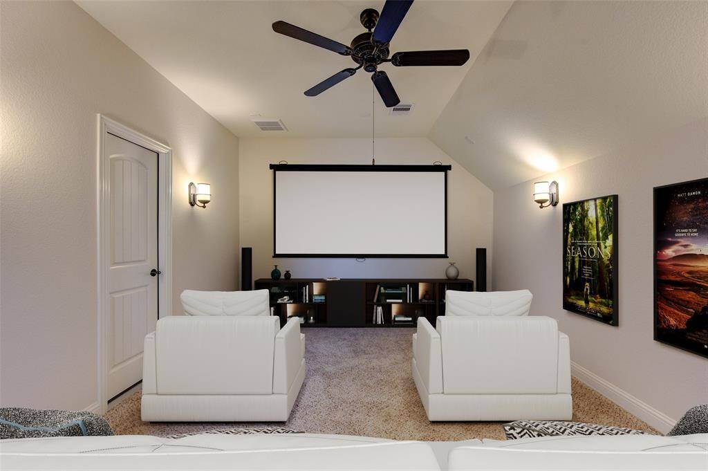 This staged home theater features cozy white seating, a large screen, and surround sound speakers, set in a carpeted room with ambient wall lighting and modern decor.