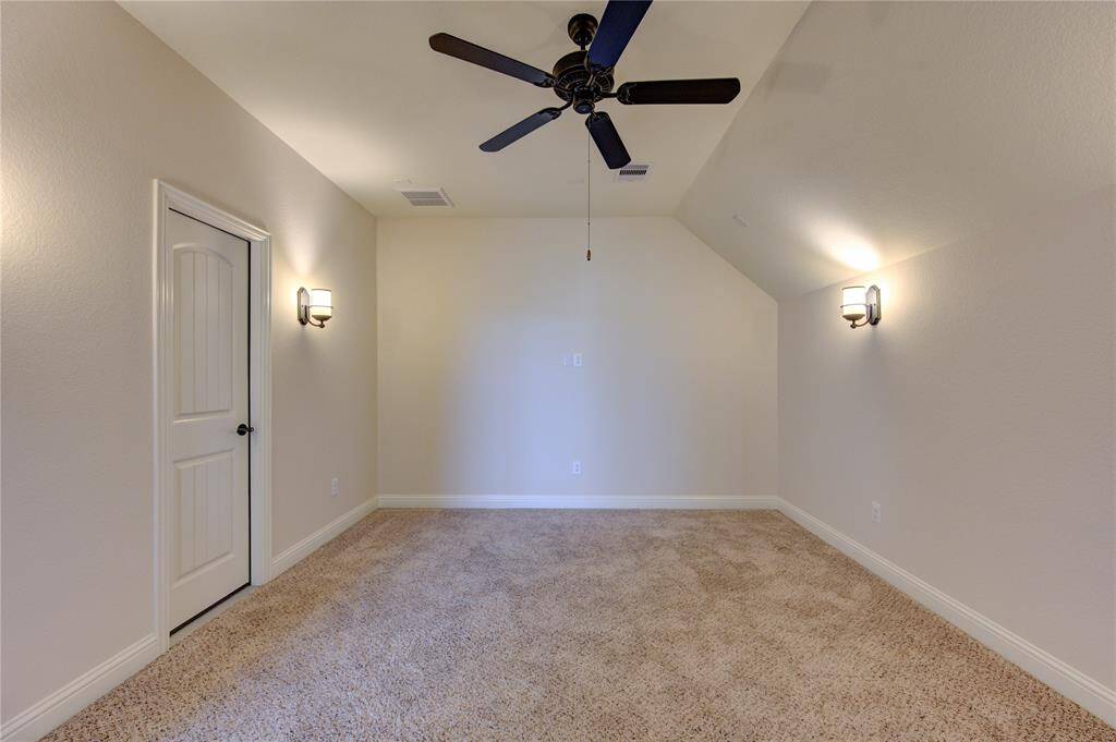 This room features a cozy carpeted floor, neutral walls, and a ceiling fan with lighting. It has a sloped ceiling and wall sconces providing soft illumination. Ideal for a home theater.