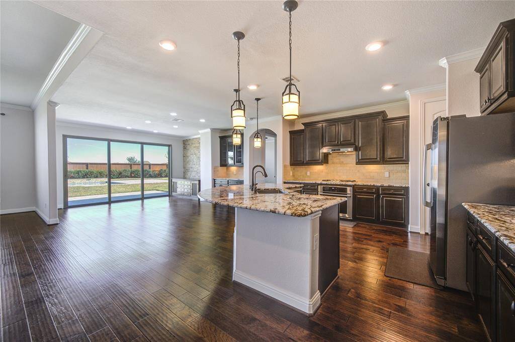 A spacious open-plan kitchen and living area with the kitchen features modern stainless-steel appliances. Large sliding glass doors offer ample natural light and lead to an outdoor space, enhancing the room's airy feel.