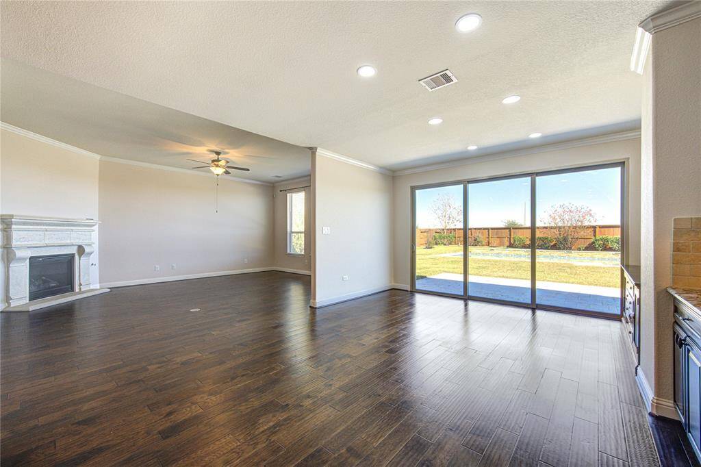 The open concept living area with dark hardwood floors, a cozy fireplace, and large sliding glass doors leading to a sunny backyard. The room is bright with recessed lighting and a ceiling fan, offering a modern and inviting atmosphere.