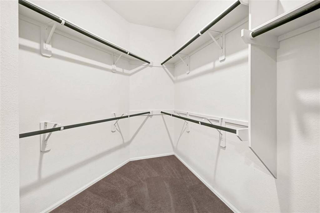 This photo shows a spacious walk-in closet with multiple hanging rods and shelves, offering ample storage space against clean white walls.