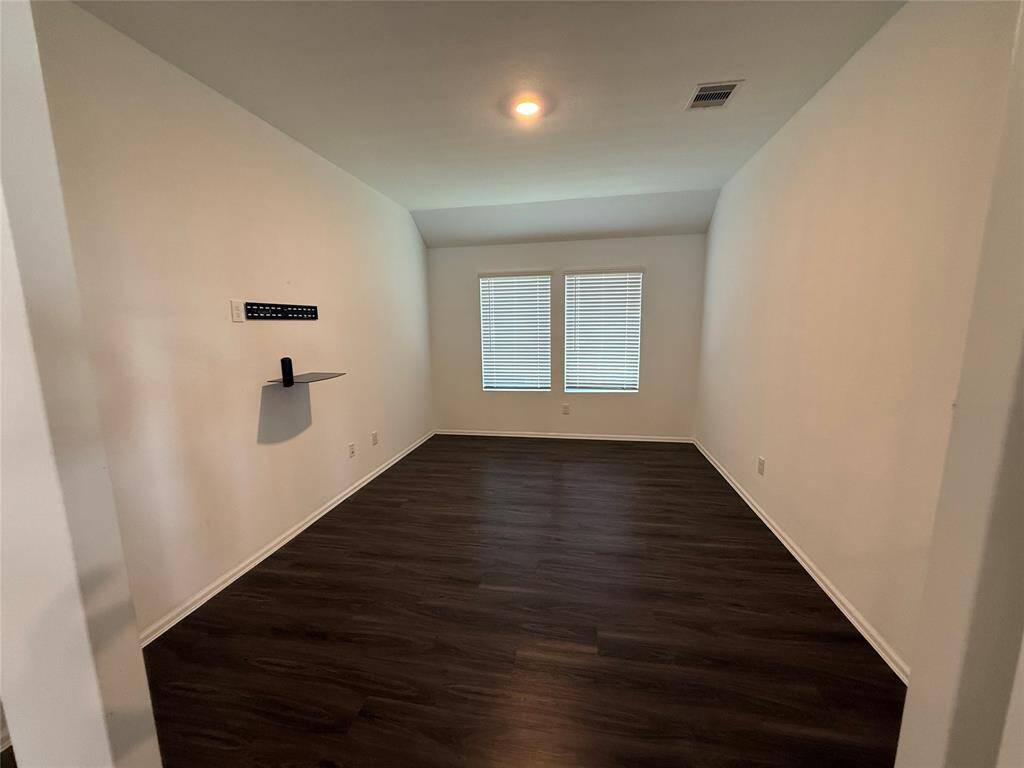 This room features dark wood flooring and neutral walls, with two windows providing natural light. It offers a modern touch and is a functional space for entertainment setup.