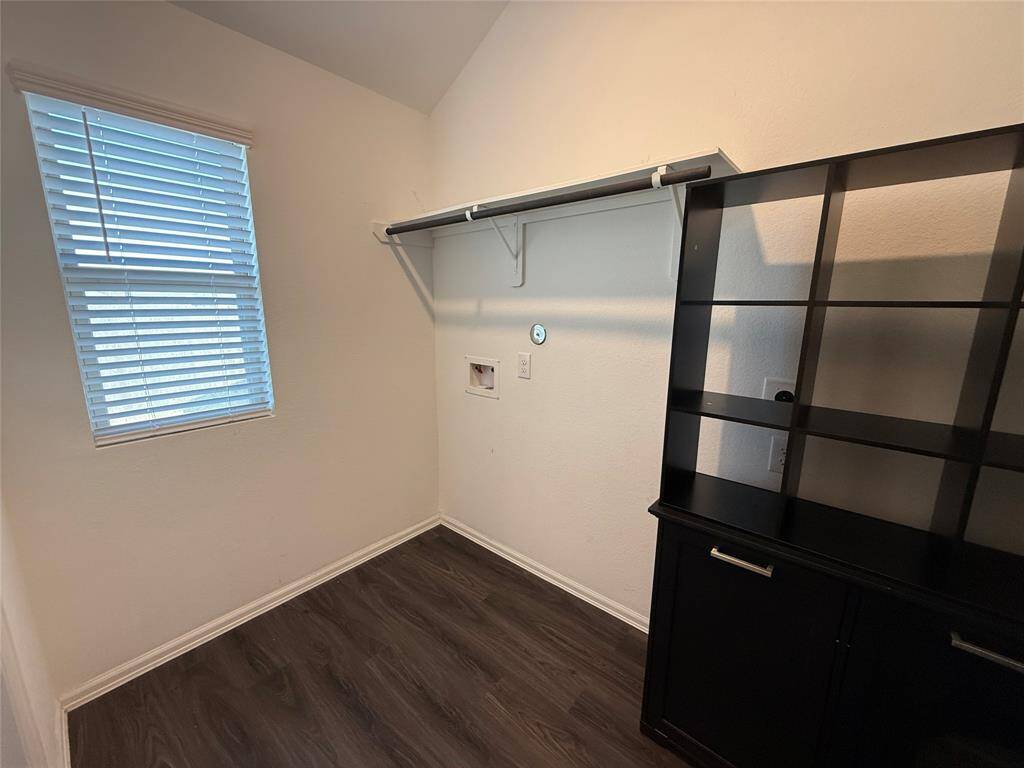 Compact utility room with a window, dark flooring, shelving, and hookups for appliances. Ideal for laundry.
