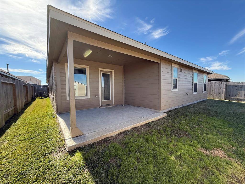 The backyard has a covered patio, enclosed by a wooden fence. The house exterior has a modern look with neutral siding and multiple windows.