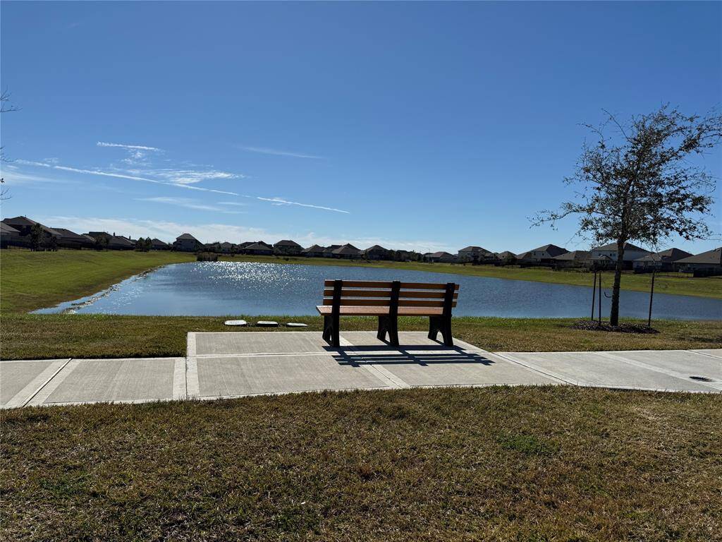 Peaceful neighborhood setting with a scenic pond view. Features a walking path and a bench for relaxation. Ideal for enjoying serene outdoor moments.