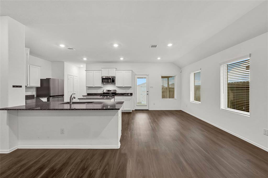 This home features a modern, open-concept kitchen and living area with sleek wooden flooring. The kitchen features white cabinetry, granite countertops, and stainless steel appliances. Large windows provide ample natural light, creating a bright and inviting space.
