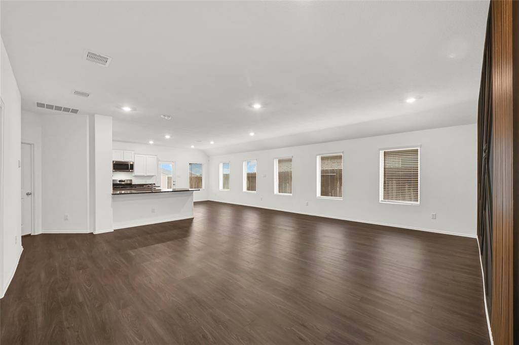 This spacious open-plan living area features dark hardwood floors & recessed lighting. Multiple windows provide ample natural light, creating a bright and inviting space ideal for entertaining.