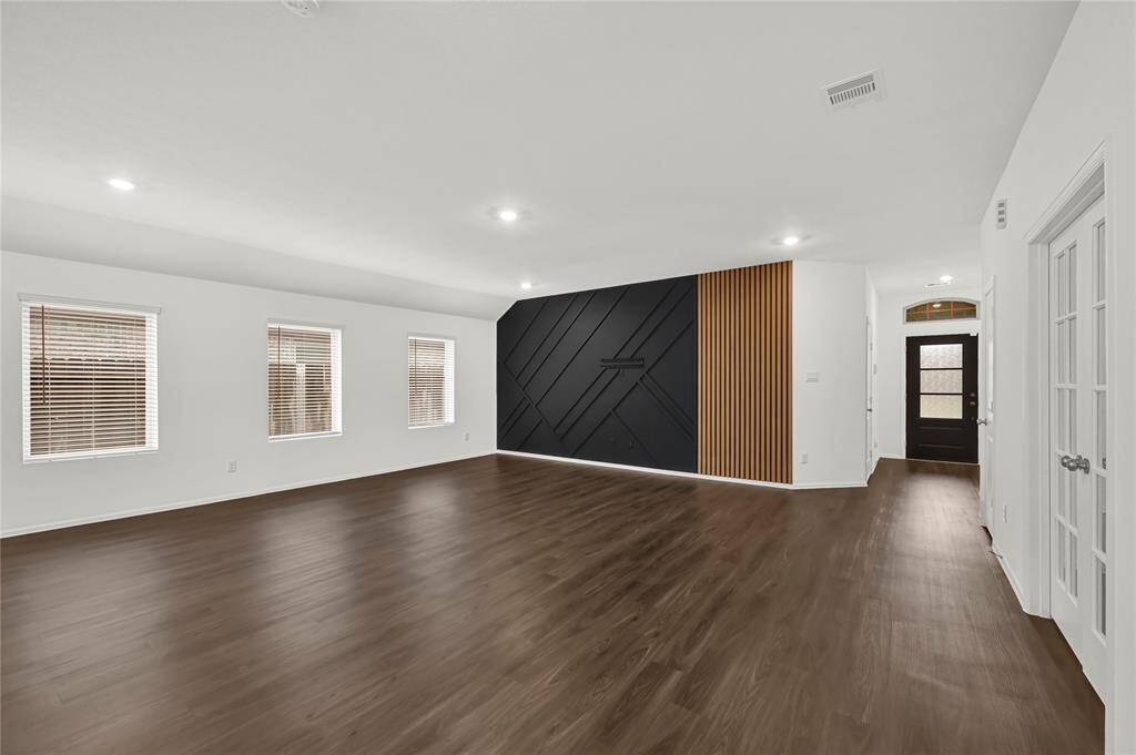 Spacious living room with a modern accent wall, and ample natural light. It also features a stylish entry door and sleek interior design elements.