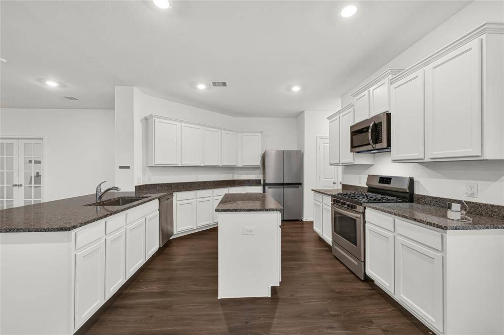 This kitchen features modern stainless steel appliances, dark granite countertops, and ample white cabinetry, complemented by a spacious island and wood flooring.