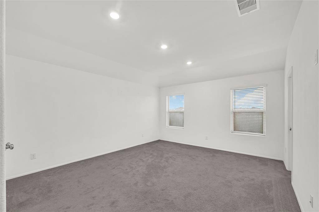 The primary bedroom features a spacious layout with neutral walls and carpeting, recessed lighting, and two windows providing ample natural light.