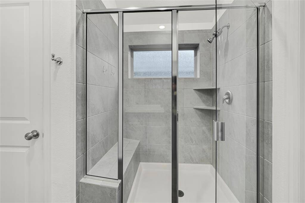 This photo features a modern, tiled shower with a glass door and a built-in bench. The shower has a small window for natural light and a sleek, minimalist design.