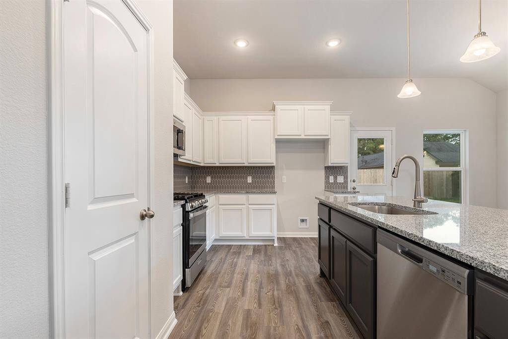 This modern kitchen features sleek granite countertops, stainless steel appliances, and ample white cabinetry. The open layout and large windows provide plenty of natural light, while wood look flooring adds warmth. A central island offers additional workspace and seating.