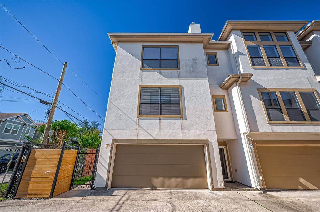 Modern four-story townhouse with a clean, stucco exterior and two-car garage. It features large windows for ample natural light. A gated entry provides added security, and the property is situated in a well-maintained neighborhood.
