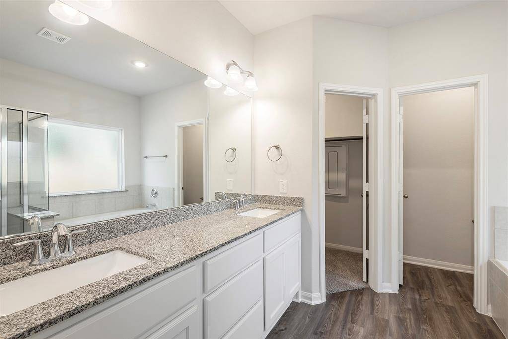 En suite features a double vanity with granite countertops, sleek fixtures, and ample under-sink storage. It has a spacious shower, a separate bathtub, and wood-look flooring for a modern touch.