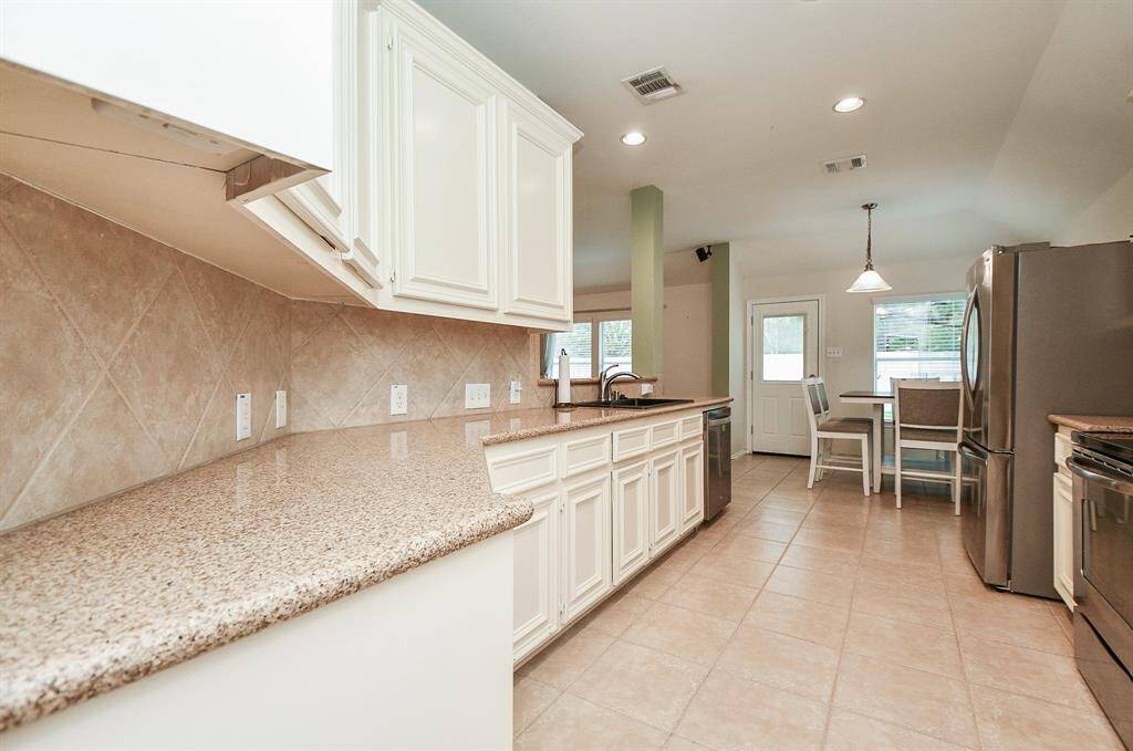 This kitchen features spacious granite countertops, white cabinetry, and stainless steel appliances. It opens to a cozy dining area with ample natural light and neutral tile flooring, creating a welcoming and functional space.