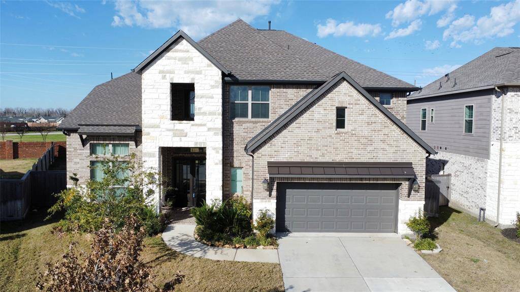This is a modern two-story brick and stone home with a gabled roof and a two-car garage. The front features a neatly landscaped yard and a welcoming entryway. It's situated in a suburban neighborhood with ample space between houses.