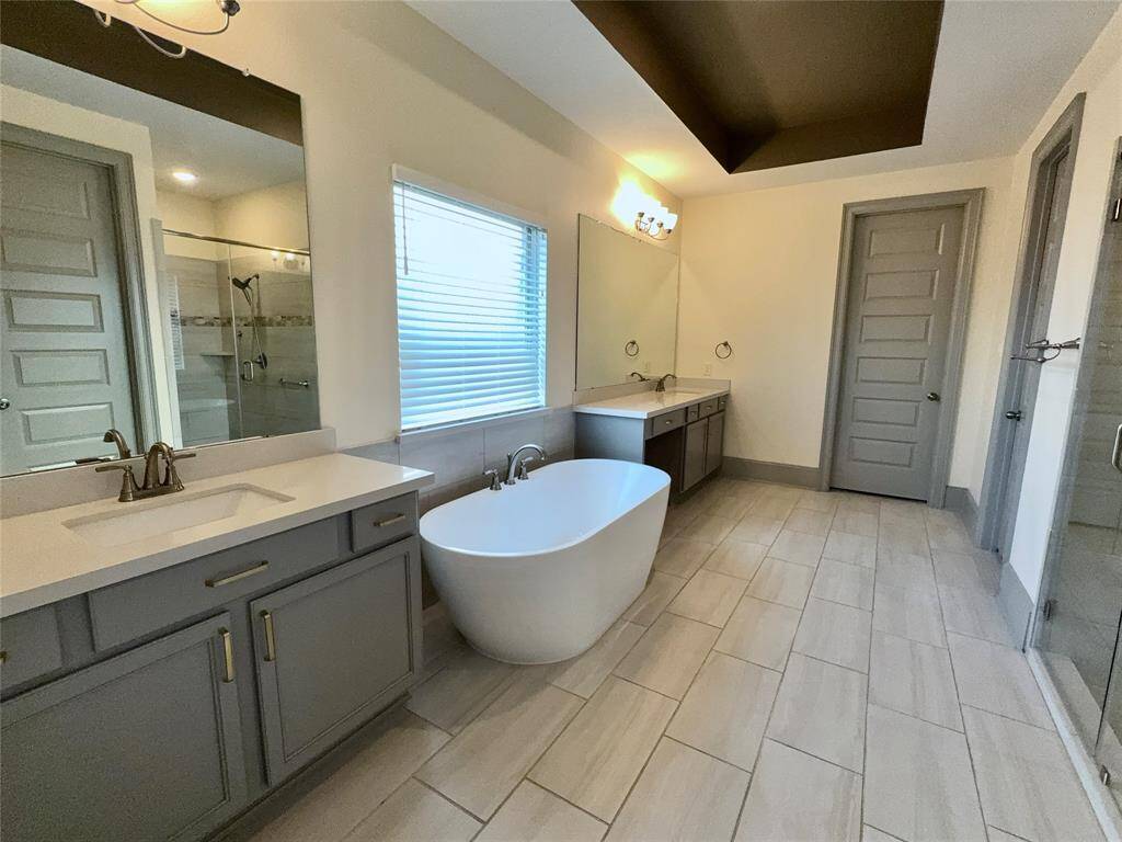 This spacious bathroom features modern fixtures, a freestanding bathtub, double vanities, and a large walk-in shower. The neutral tones and ample lighting create a relaxing atmosphere.