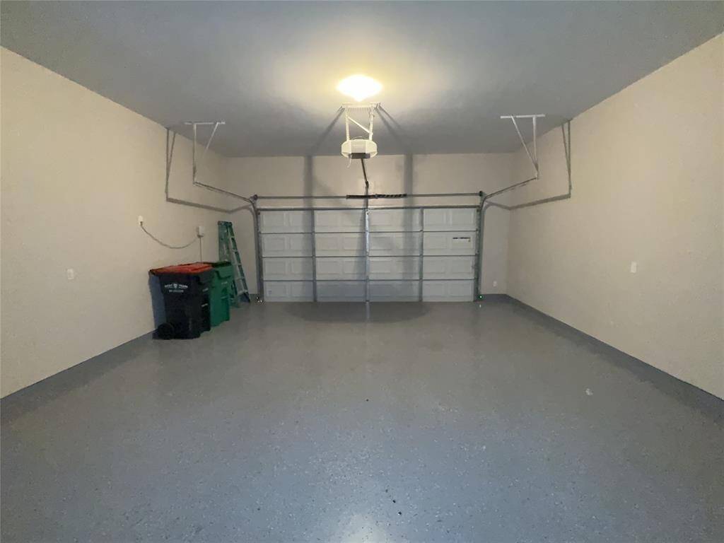 Spacious two-car garage with a clean, finished floor and ample overhead lighting. It includes a mounted garage door opener and room for storage on the sides.