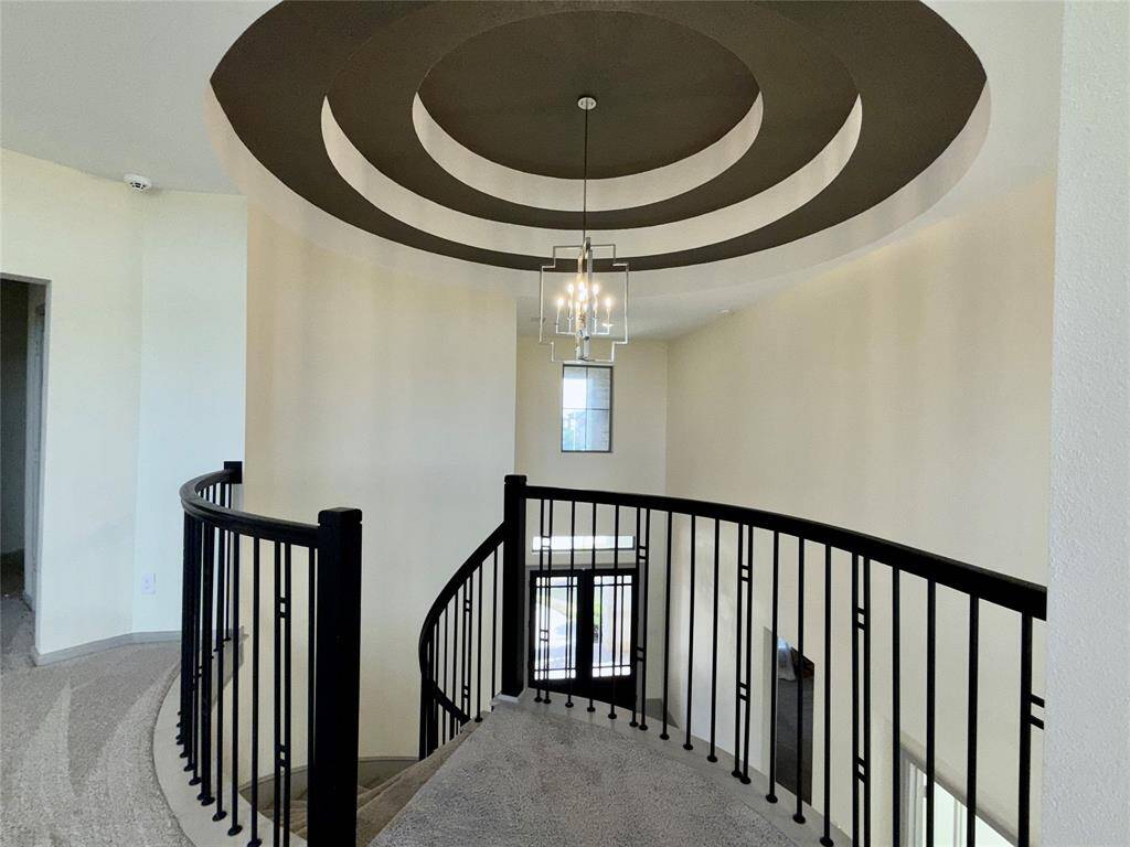 Modern, curved staircase with elegant black railings and plush carpeting. The ceiling features a stylish concentric circle design with a central light fixture, adding a touch of sophistication to the space.