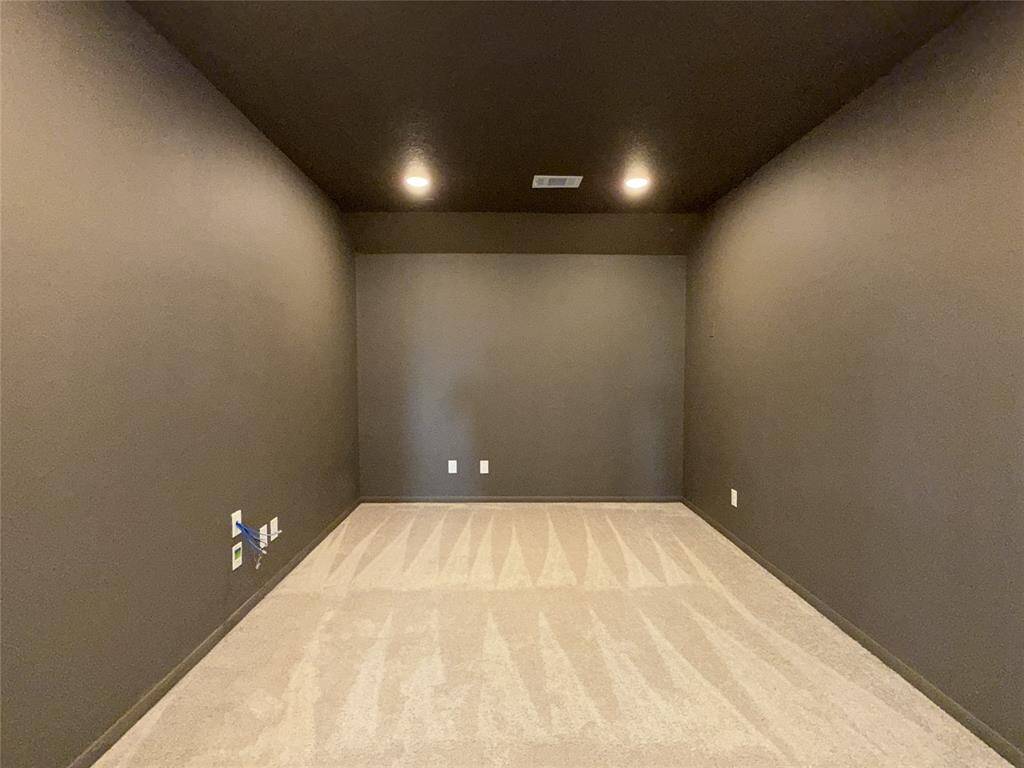 Media room features dark walls and ceiling, creating a cozy atmosphere, perfect for a media or entertainment space. It has built-in lighting and outlets, with carpeted flooring, offering a versatile space for customization.