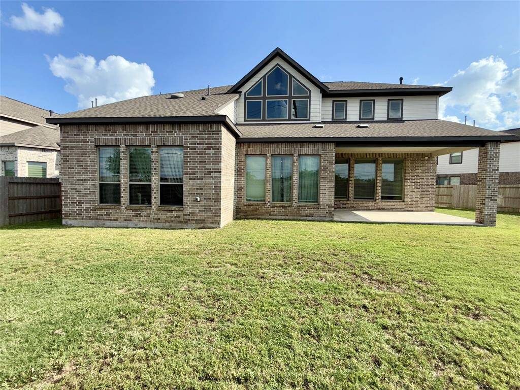 Spacious two-story brick house with large windows, a covered patio, and a well-maintained grassy backyard, ideal for outdoor activities.