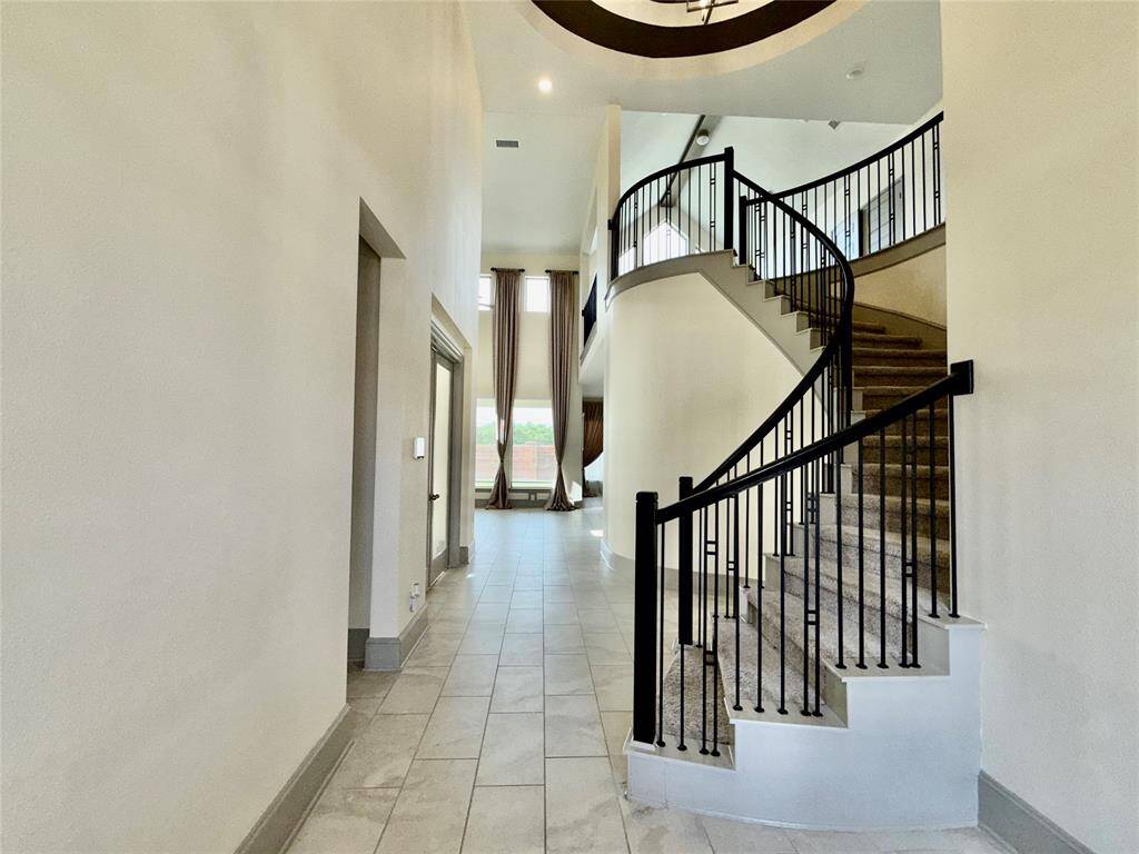 Spacious foyer with a grand spiral staircase featuring elegant black railings. The area is well-lit with natural light from tall windows and features neutral-toned tile flooring, creating a welcoming and modern entrance.