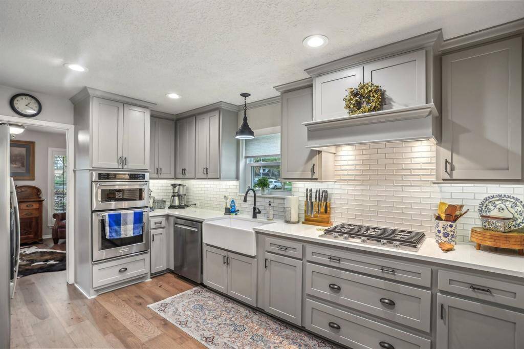 This kitchen features modern gray cabinetry, stainless steel appliances, and a farmhouse sink. The white subway tile backsplash and ample counter space provide a clean, contemporary look. Warm wood floors and under-cabinet lighting create an inviting atmosphere.